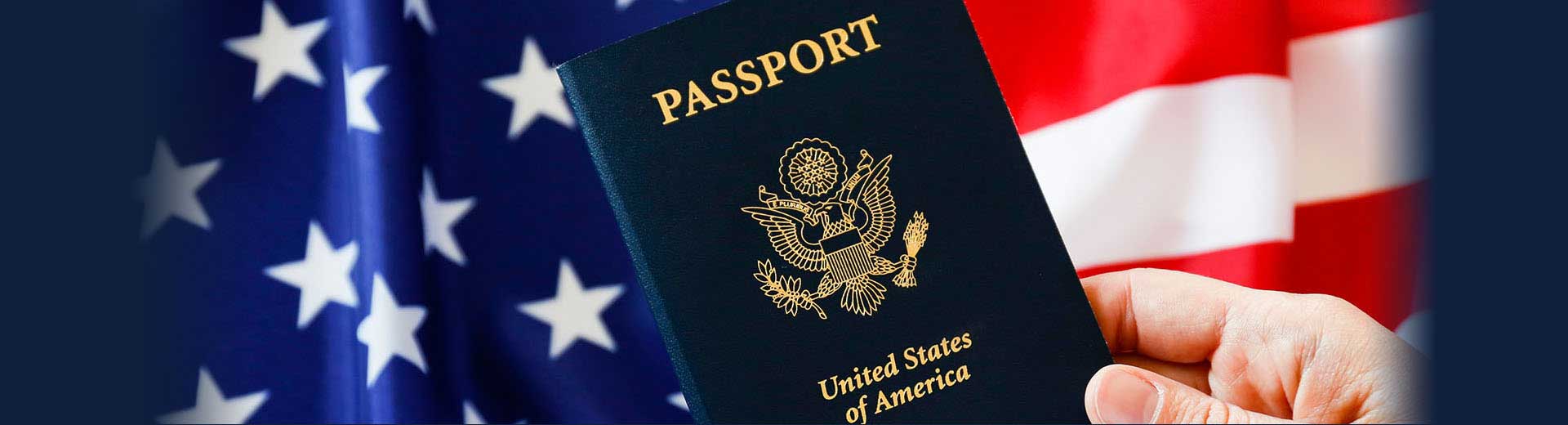 A hand holding a U.S. passport with an American flag in the background.
